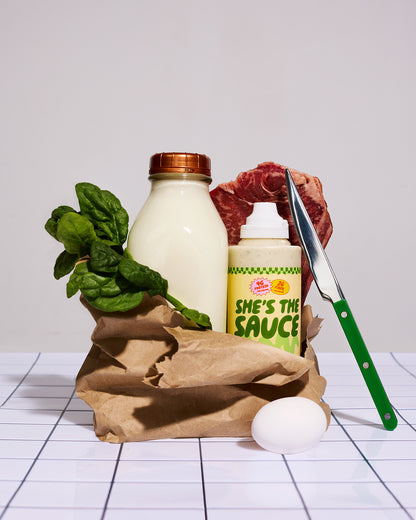 Grocery items including milk, spinach, meat, a bottle labeled 'She's the Sauce Creamy Ranch', an egg, and a knife on a white surface.