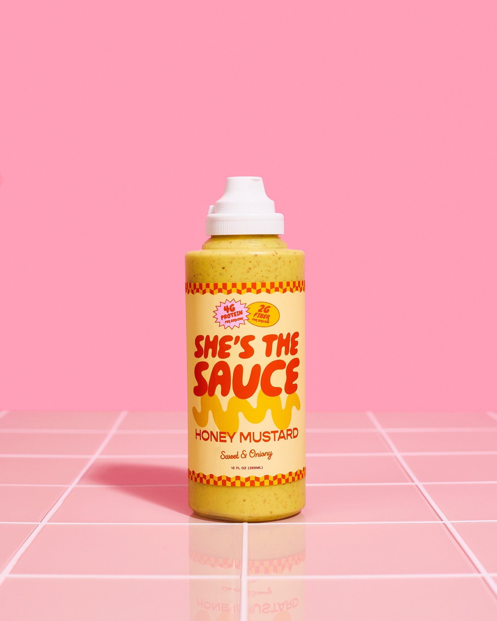 Bottle of She's the Sauce Honey Mustard on a pink grid background