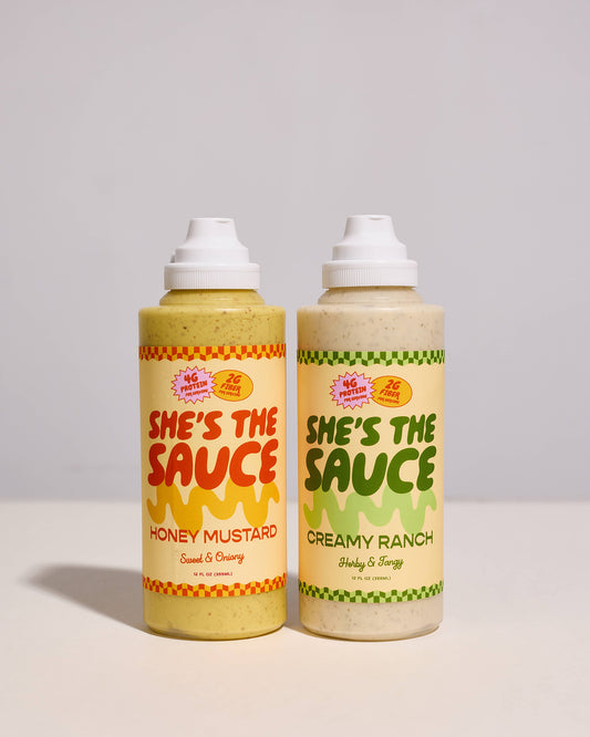 Two bottles of 'She's the Sauce' on a gray background